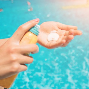 Une personne met de la crème solaire dans sa main, devant une piscine