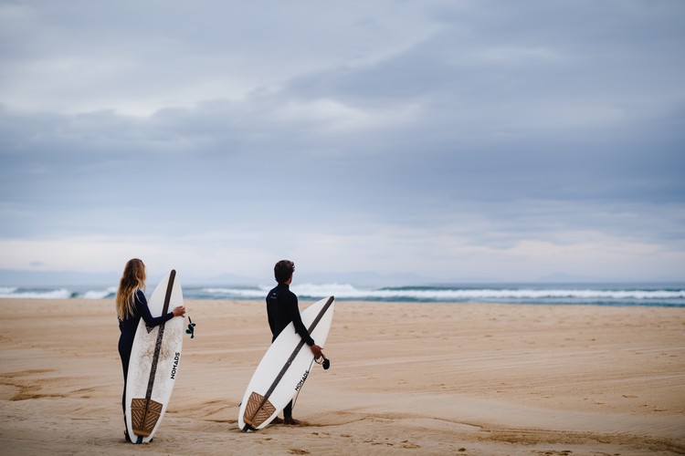 Deux personnes faces à l'océan avec des surfs Nomads
