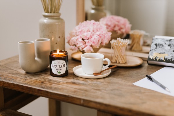 Bougie La Belle Mèche allumée sur une table avec d'autres objets de déco et une tasse de café